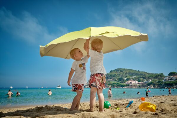 two children playing under umbrella on seashore